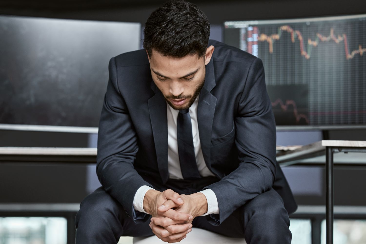 Man thinking on front of screens showing candlestick charts